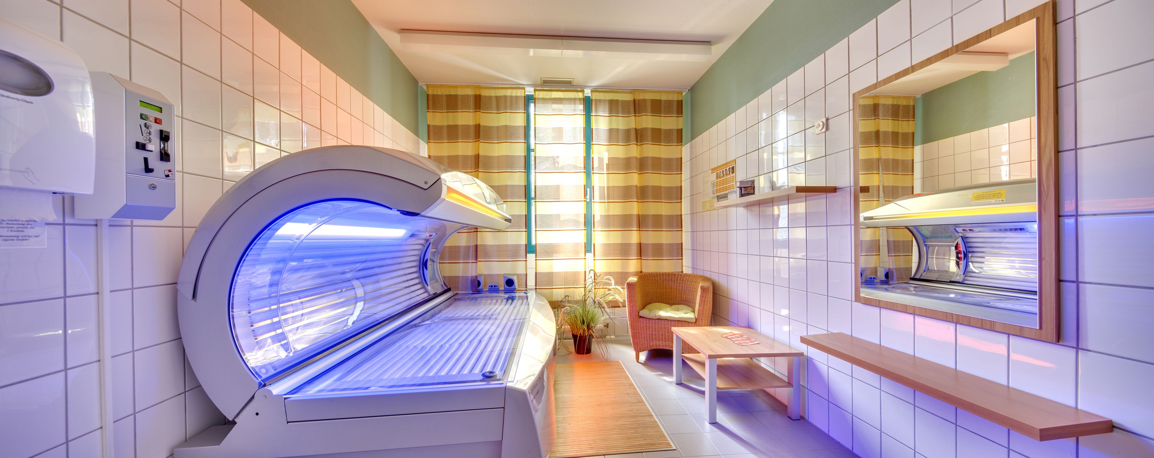 A room with a tanning bed, a chair, a small table, and a mirror.