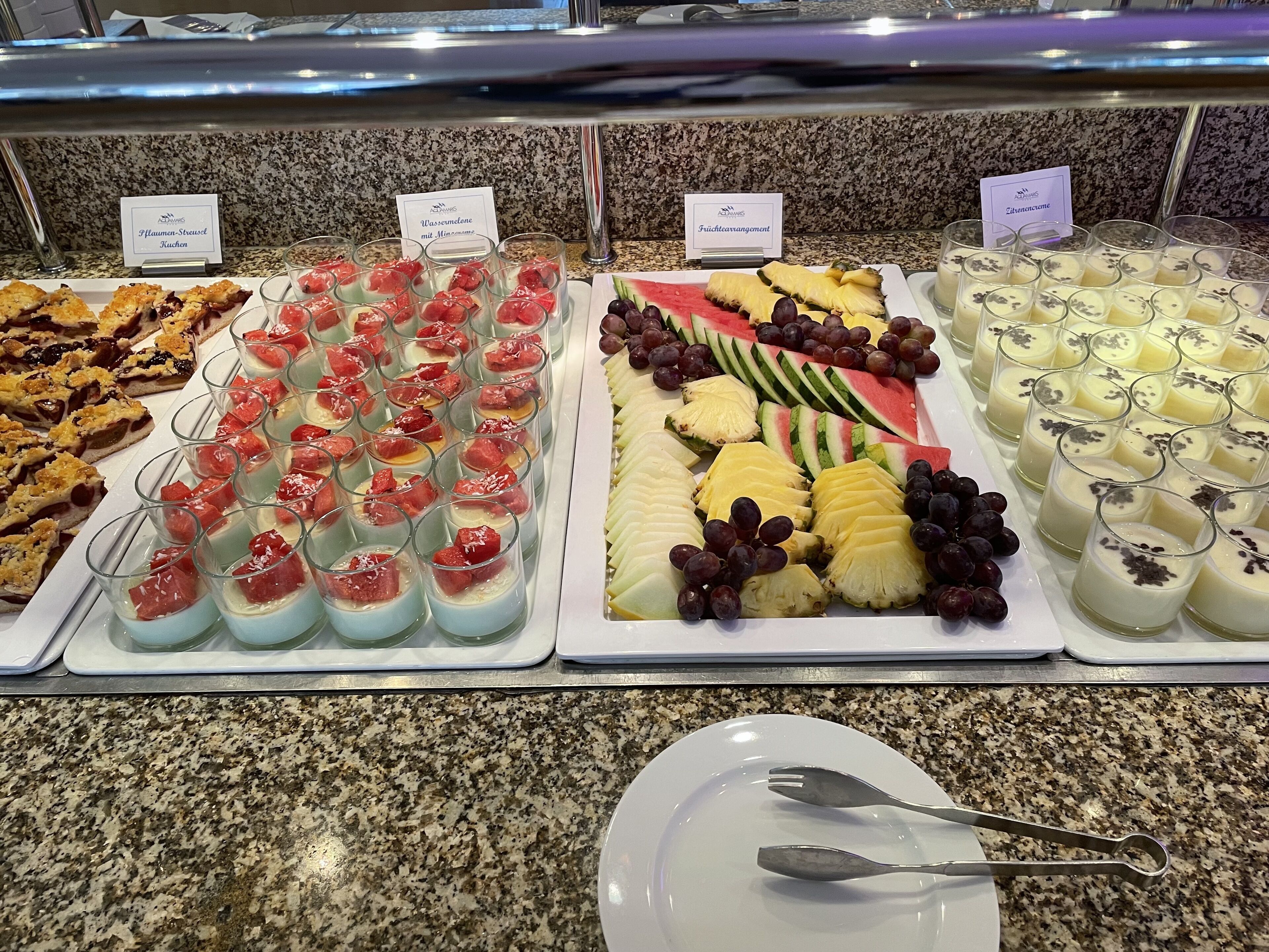 A buffet with various food items including desserts, fruits, and a plate with utensils.