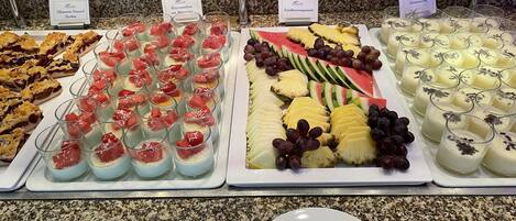 A buffet with various food items including desserts, fruits, and a plate with utensils.