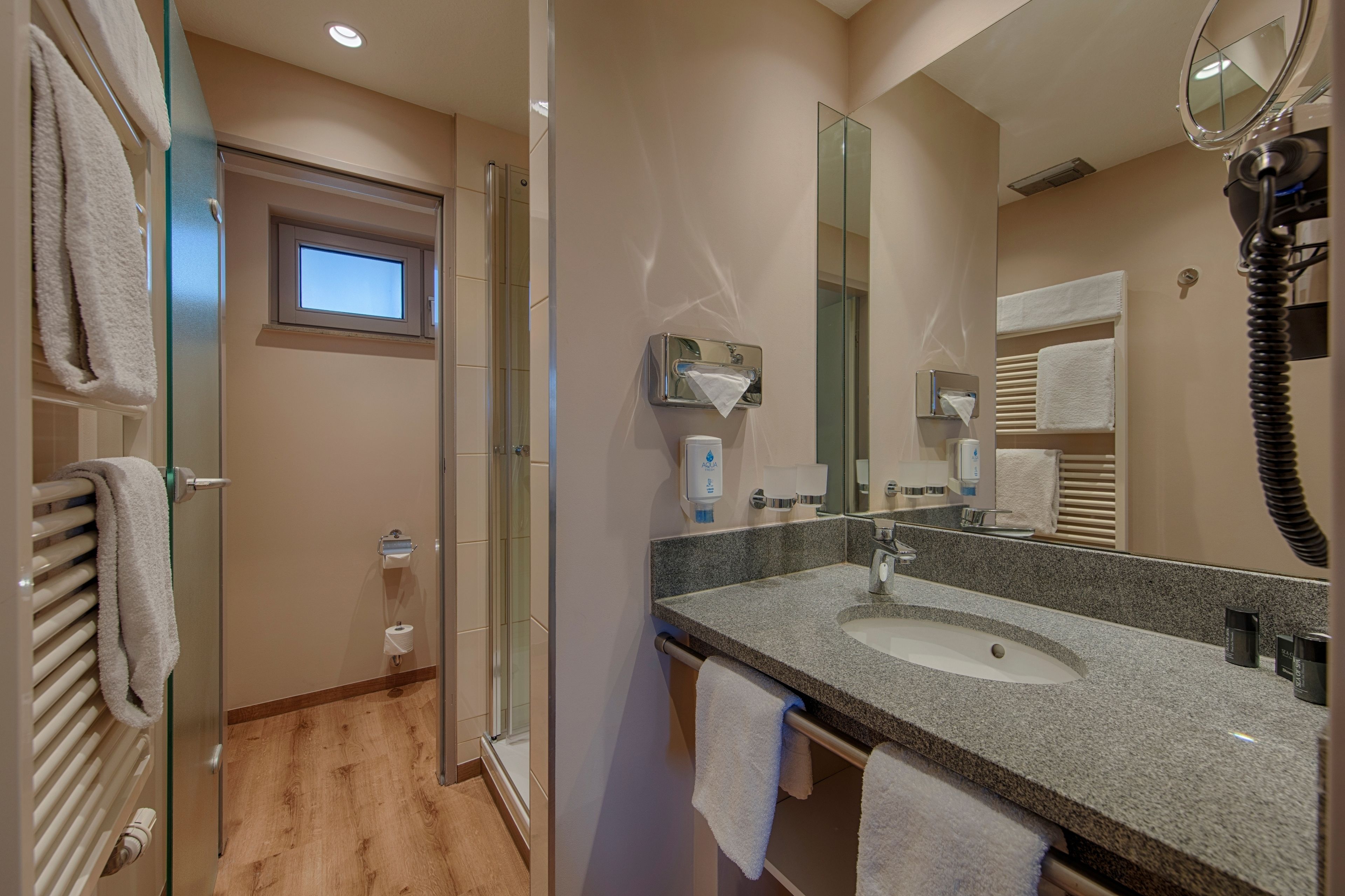 A modern bathroom with a glass shower enclosure, a granite sink, and a large mirror.