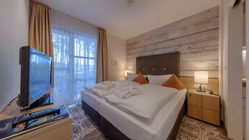 Een hotelkamer met een groot bed, een televisie, een nachtkastje met een lamp en uitzicht op bomen.