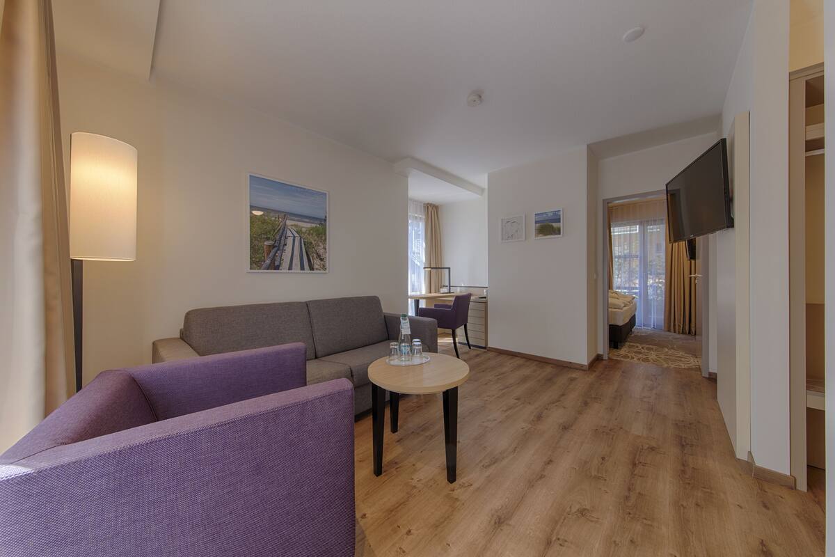 A modern living room with a sofa, a small round table, and a flat-screen TV mounted on the wall.