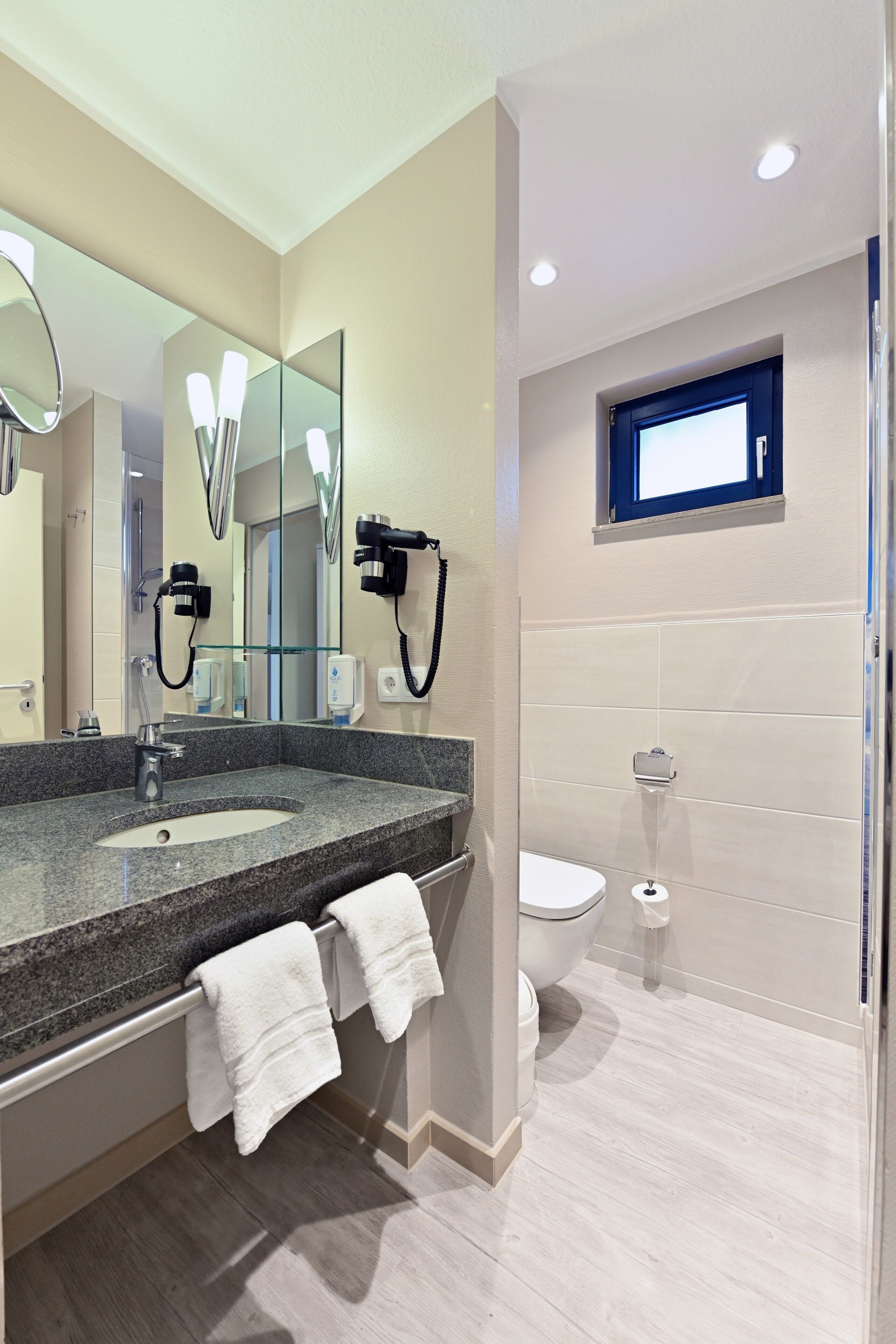 Un baño moderno con encimera de granito, un espejo grande, un secador de pelo y un inodoro.
