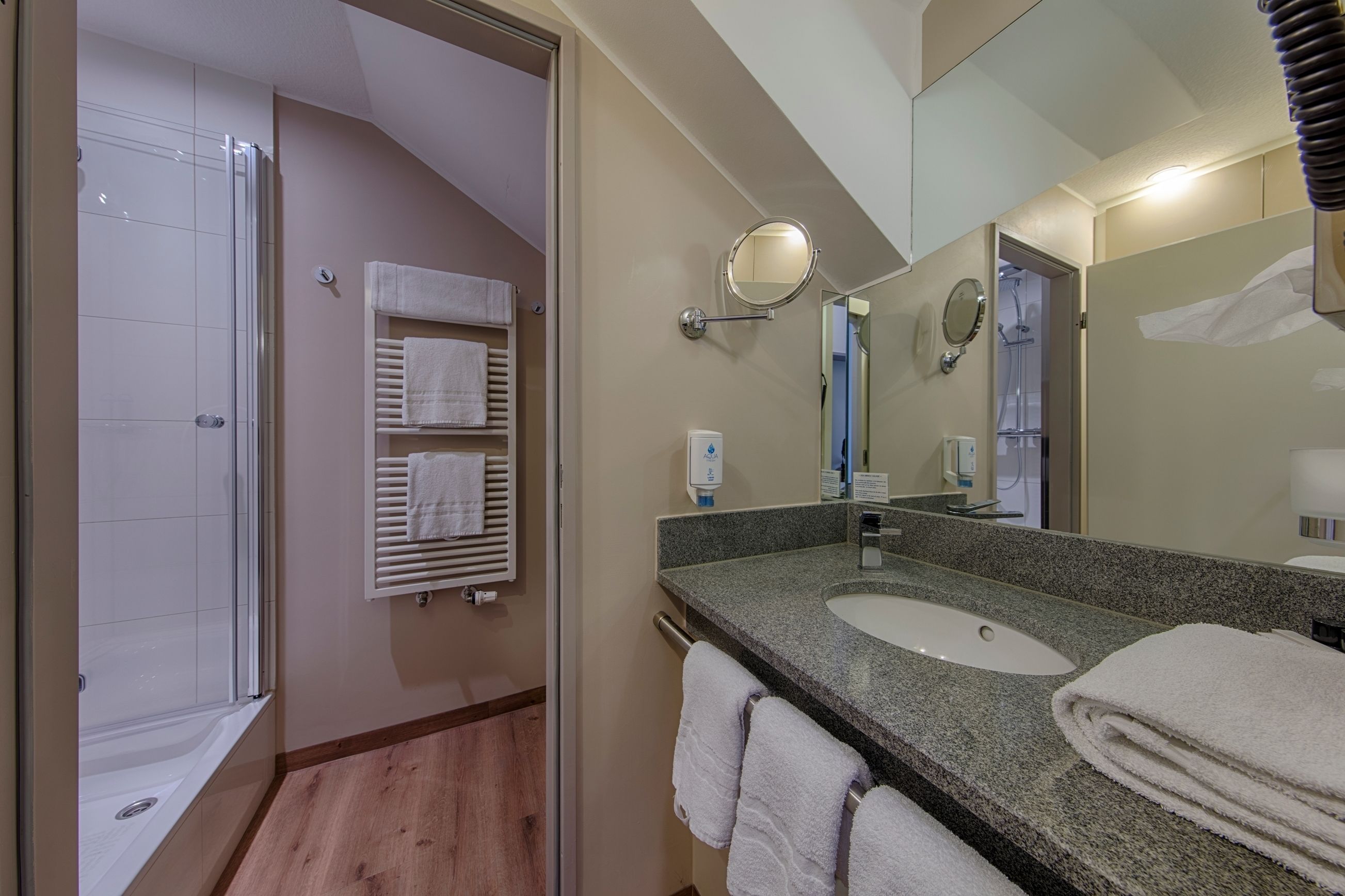 A modern bathroom with a glass shower enclosure, two sinks, and a large mirror.