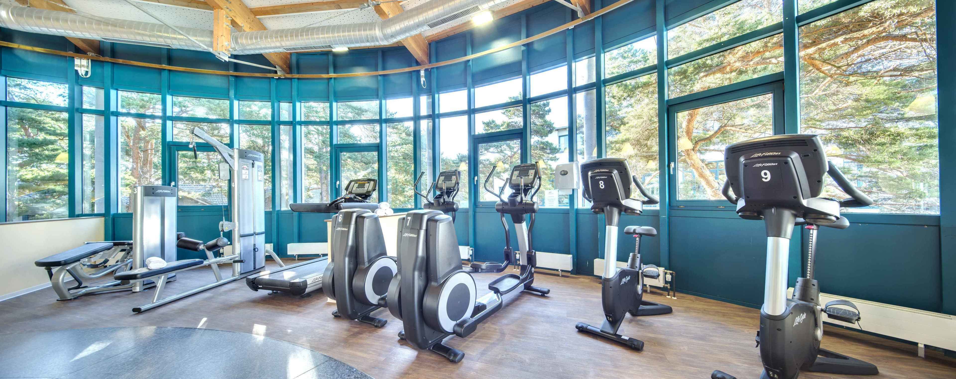 A gym with exercise equipment, large windows, and a wooden ceiling.
