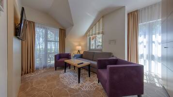 Ein modernes Hotelzimmer mit einer Couch, zwei Sesseln, einem kleinen Tisch und einem an der Wand montierten Fernseher.