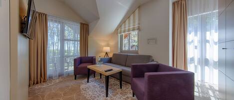 A modern hotel room with a sofa, two armchairs, a small table, and a TV mounted on the wall.