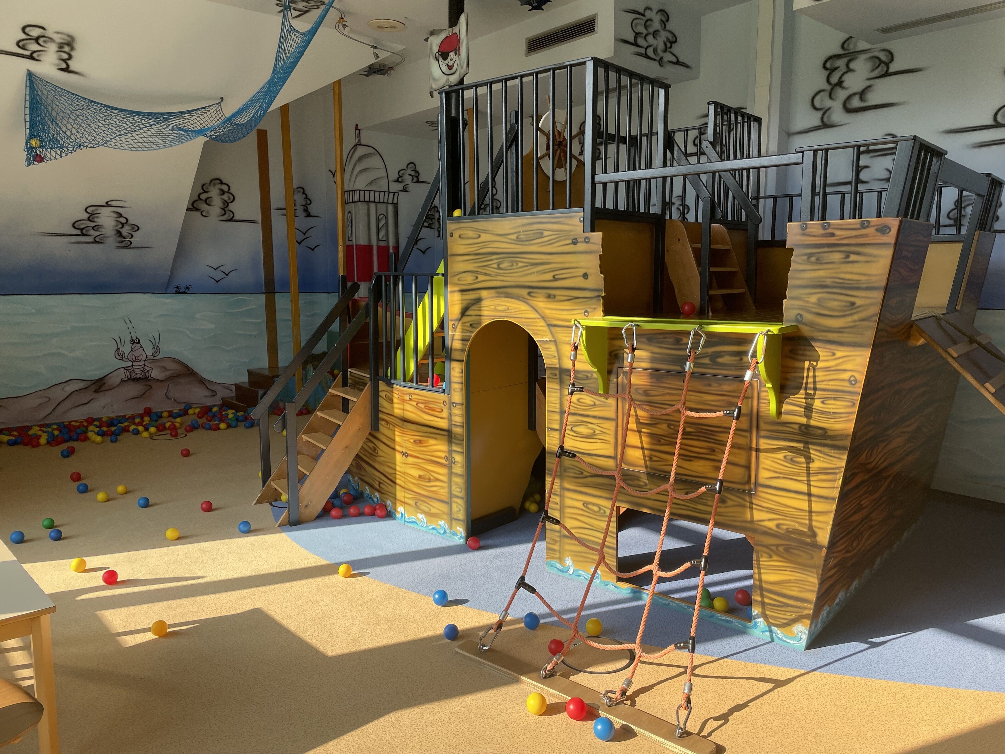 A play area with a wooden climbing structure, a slide, and a netted playpen.