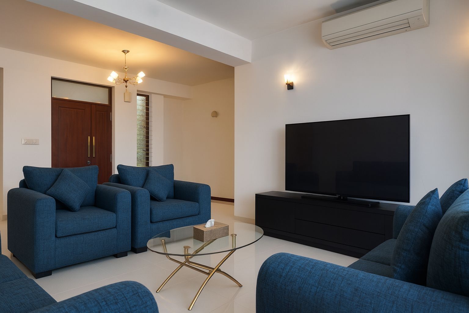 A modern living room with two blue sofas, a glass coffee table, a flat-screen TV, and a dark entertainment unit.