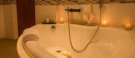 A bathroom with a large bathtub, two candles, and a showerhead.