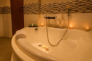 A bathroom with a large bathtub, two candles, and a showerhead. - Unique Towers Luxury Boutique Suites (Colombo)