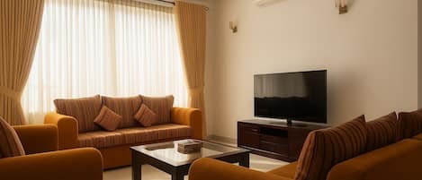 A modern living room with a sofa set, a coffee table, a flat-screen TV, and a ceiling fan.