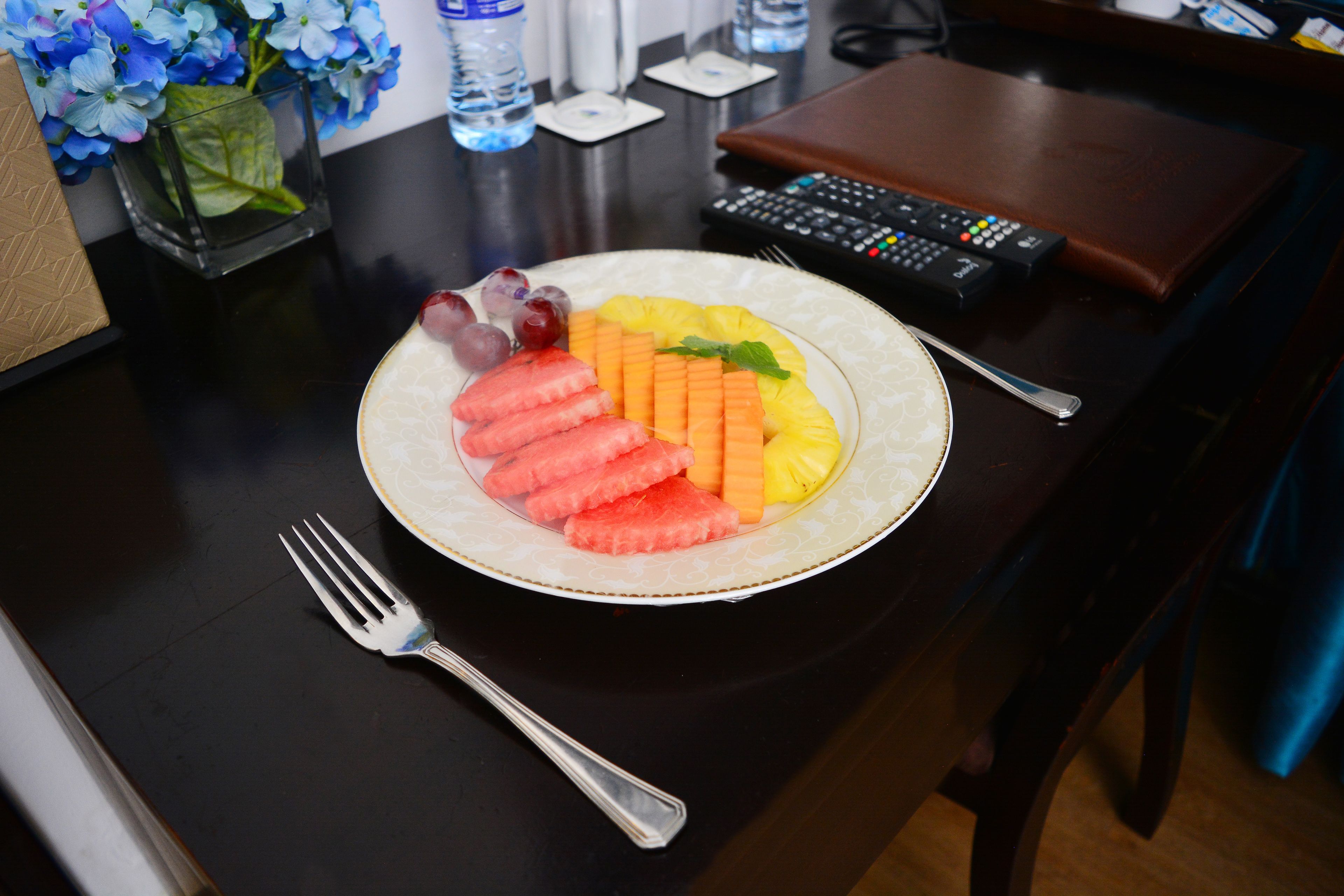 A plate of fruit on a table with a remote control and a wallet nearby.