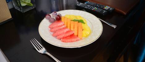 Un plato de fruta sobre una mesa, con un control remoto y una billetera cerca.