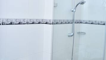 A bathroom with a glass shower enclosure, white tiles, and a black and white patterned border.