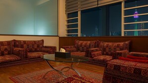 Un salon avec des canapés à motifs, une table basse en verre et une grande fenêtre donnant sur le paysage urbain.