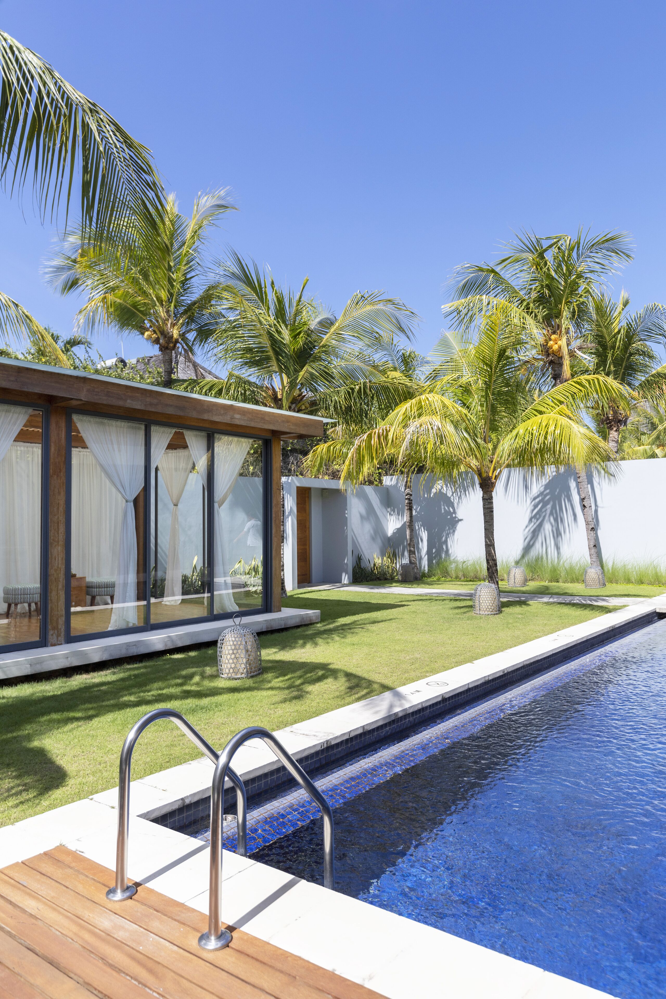 Un área de piscina moderna con terraza de madera, piscina azul cristalina y palmeras.