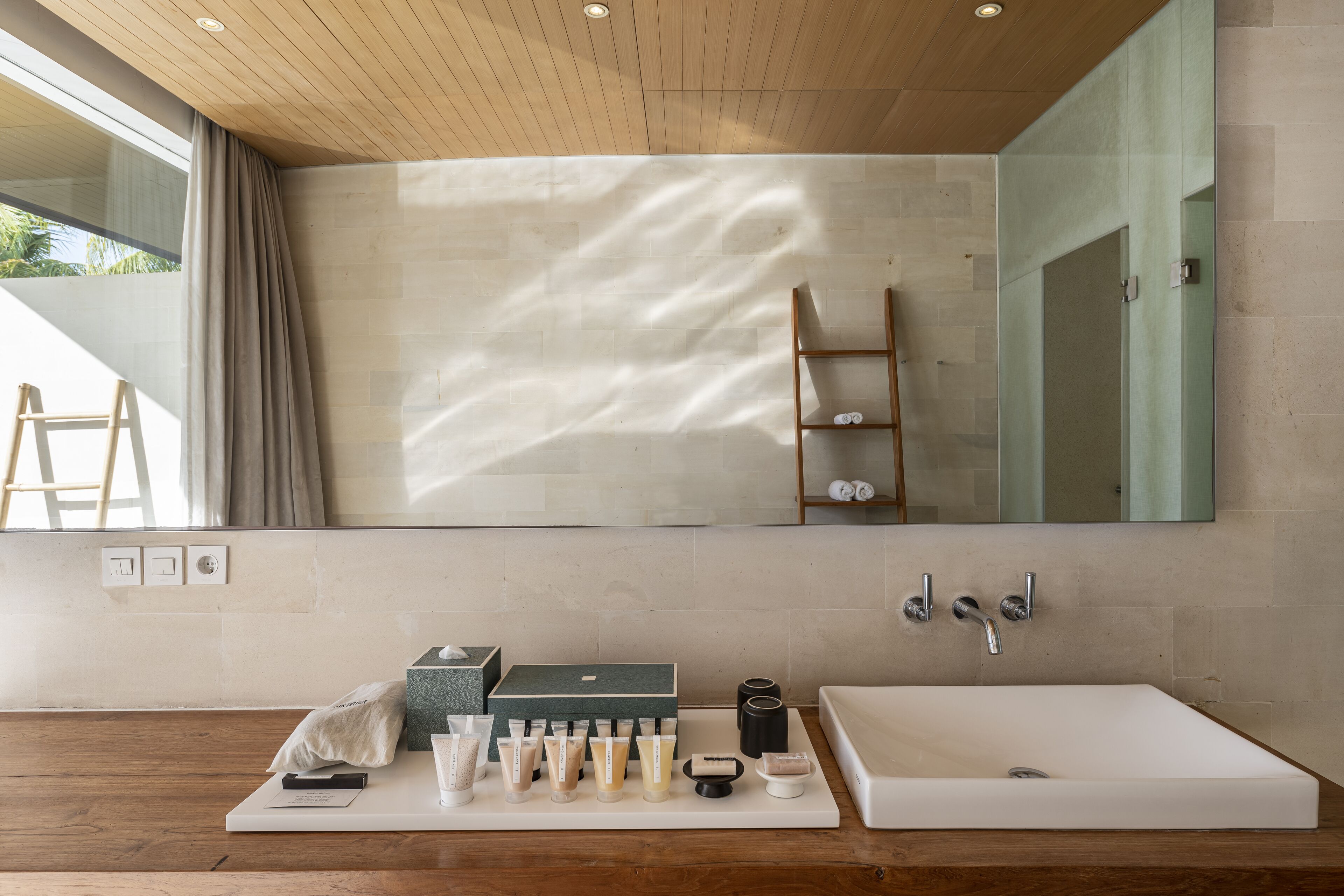 A modern bathroom with a large mirror, wooden ceiling, and a white bathtub.