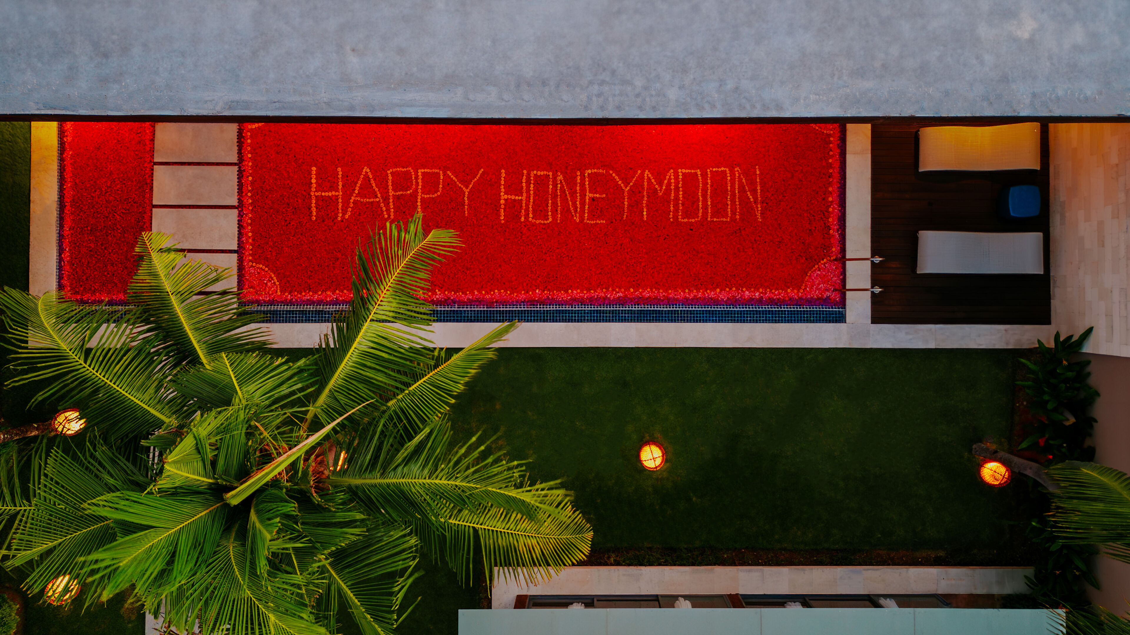 A red banner with "HAPPY HONEYMOON" text, a pool area with palm trees, and a tiled wall.