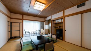 Perinteinen japanilainen huone, jossa on tatamimatto, matala pöytä tyynyineen, televisio ja liukuvat ovet.