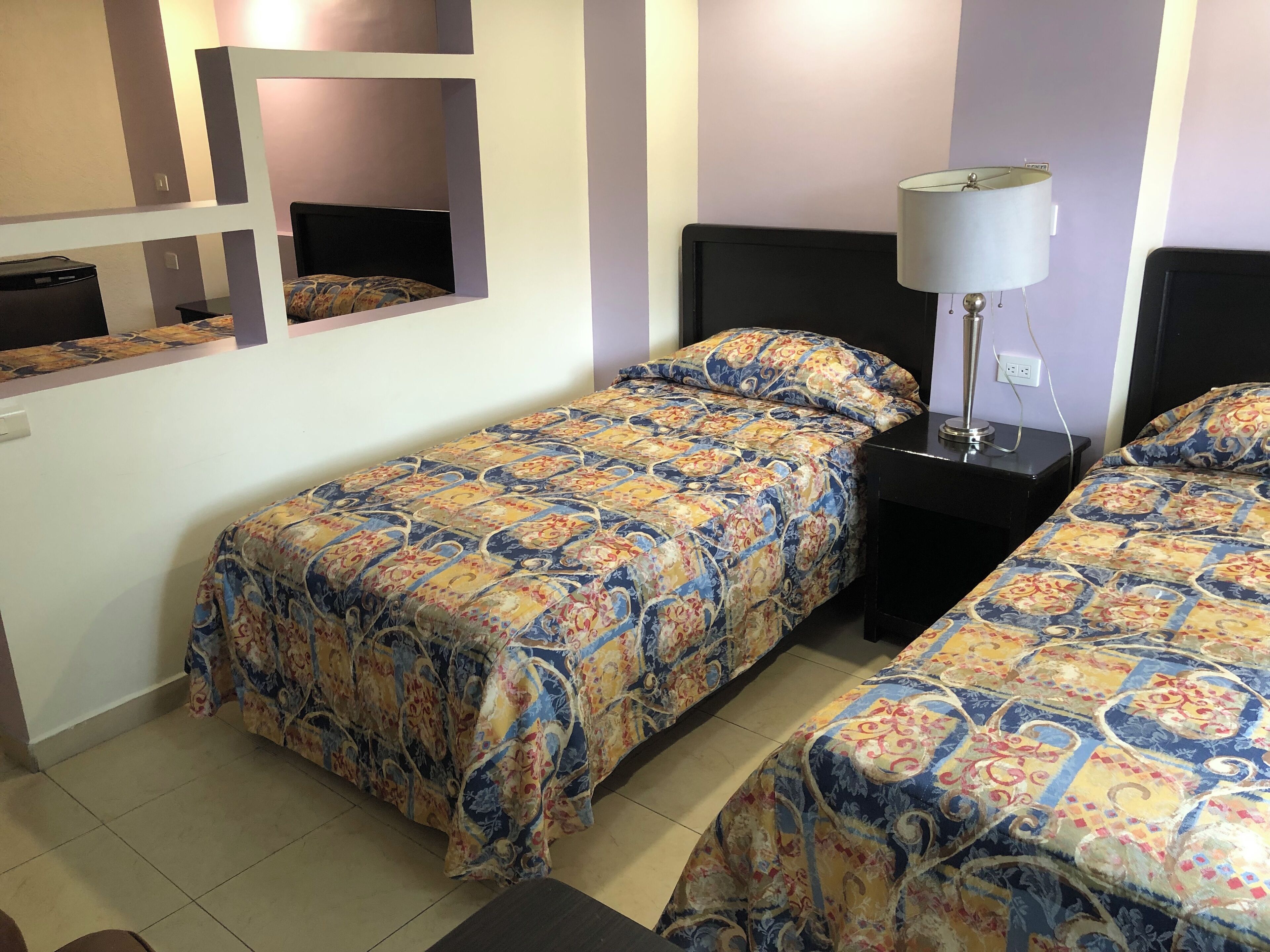 Una habitación de hotel con dos camas, un escritorio, una lámpara y un espejo.