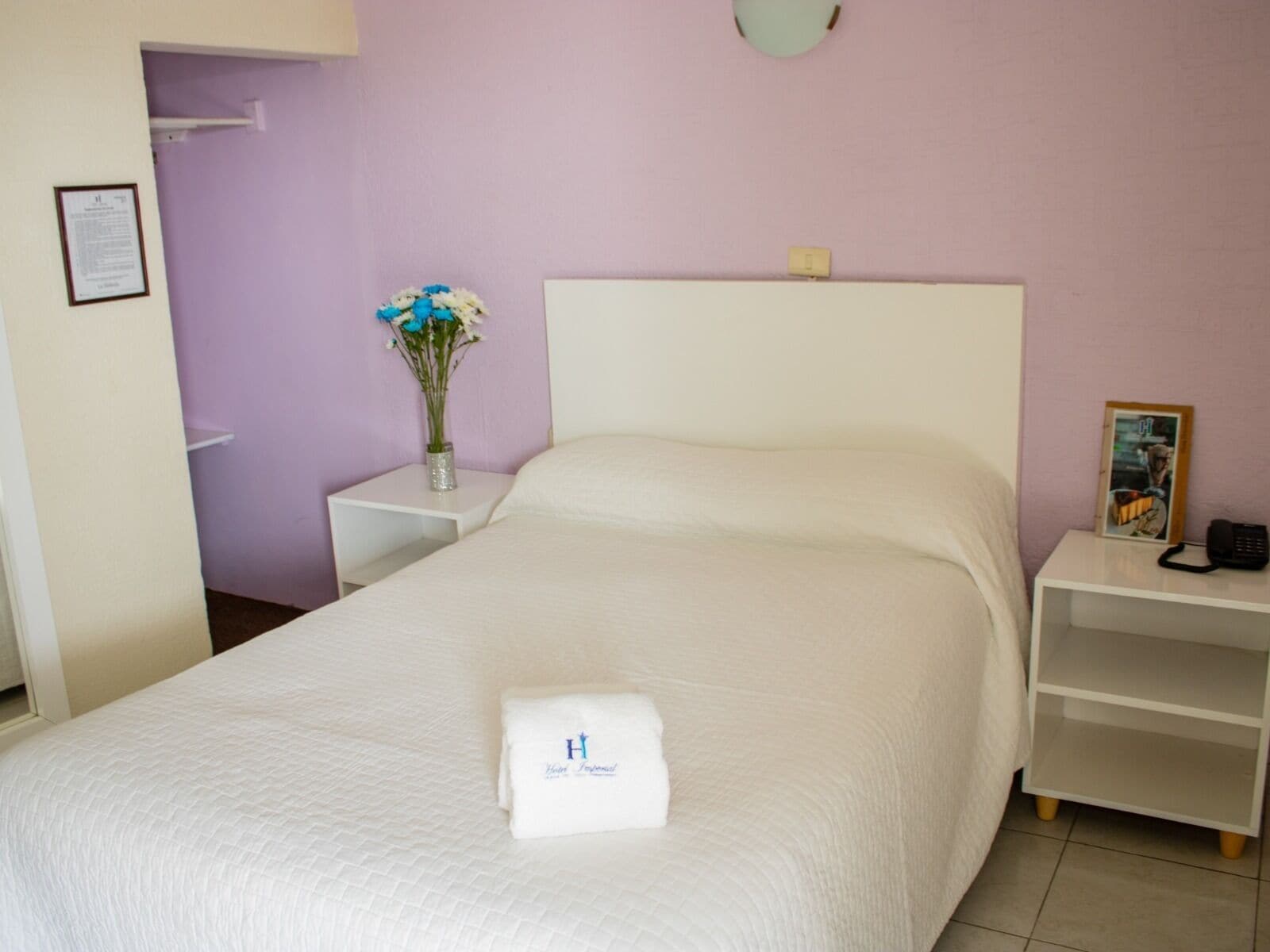 Una cama bien hecha con edredón blanco y una toalla doblada con un logo.