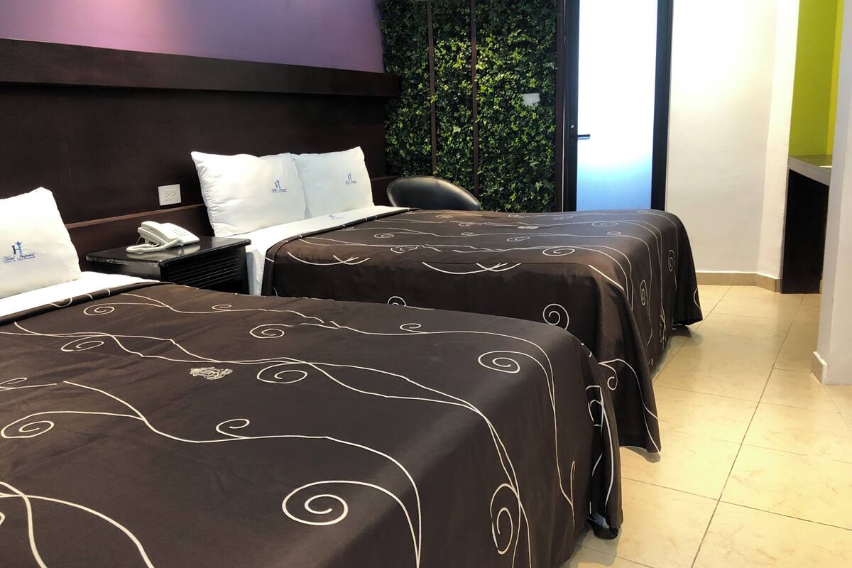 A hotel room with two beds, a desk with a phone, a chair, and a wall with greenery.