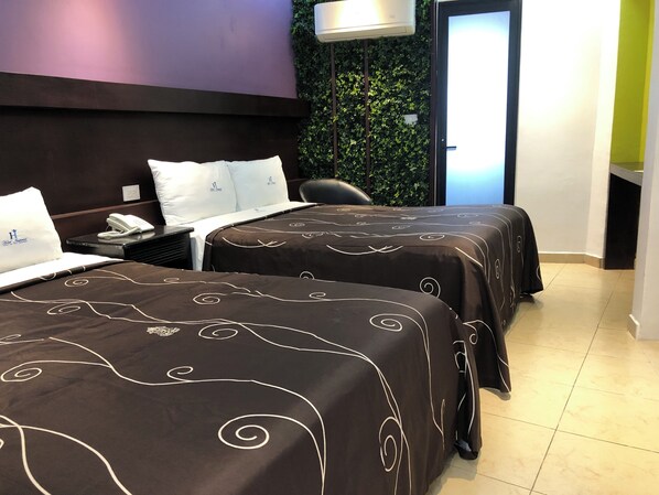Una habitación de hotel con dos camas, un escritorio con teléfono, una silla y una pared con plantas.