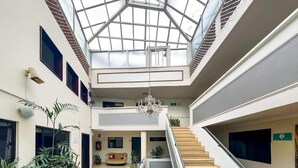 Tilava aula, jossa on keskeisellä paikalla sijaitseva portaikko, suuri kattokruunu ja korkea katto, jossa on kattovalokuvioita.