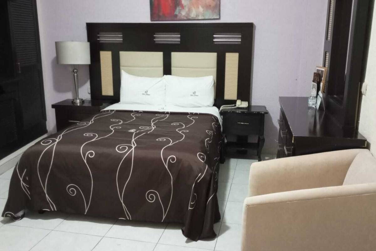 A hotel room with a bed, a nightstand, a lamp, a chair, and a desk.