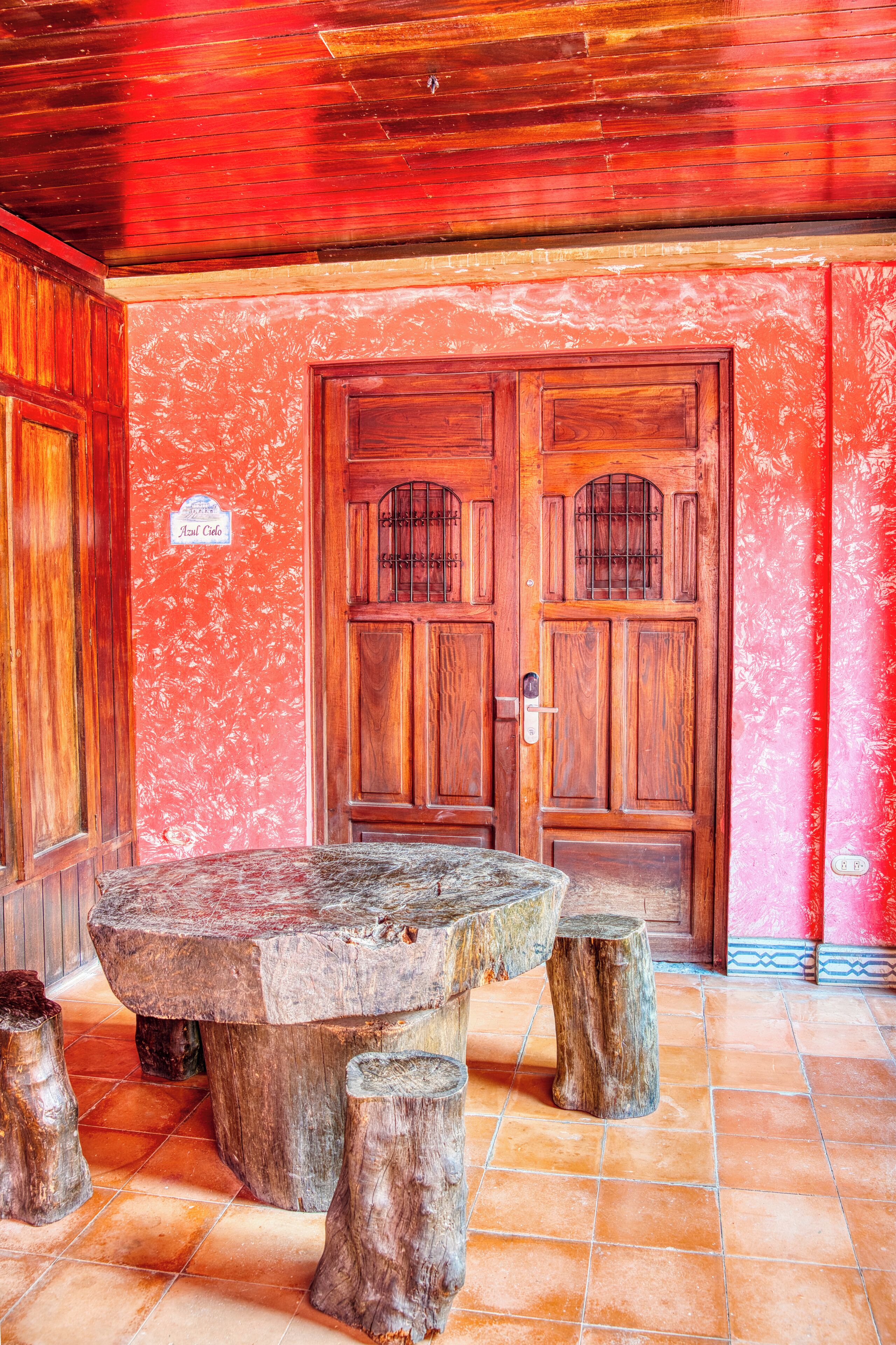 Una puerta de madera con un letrero, una mesa de piedra y troncos de madera sobre un suelo de baldosas.