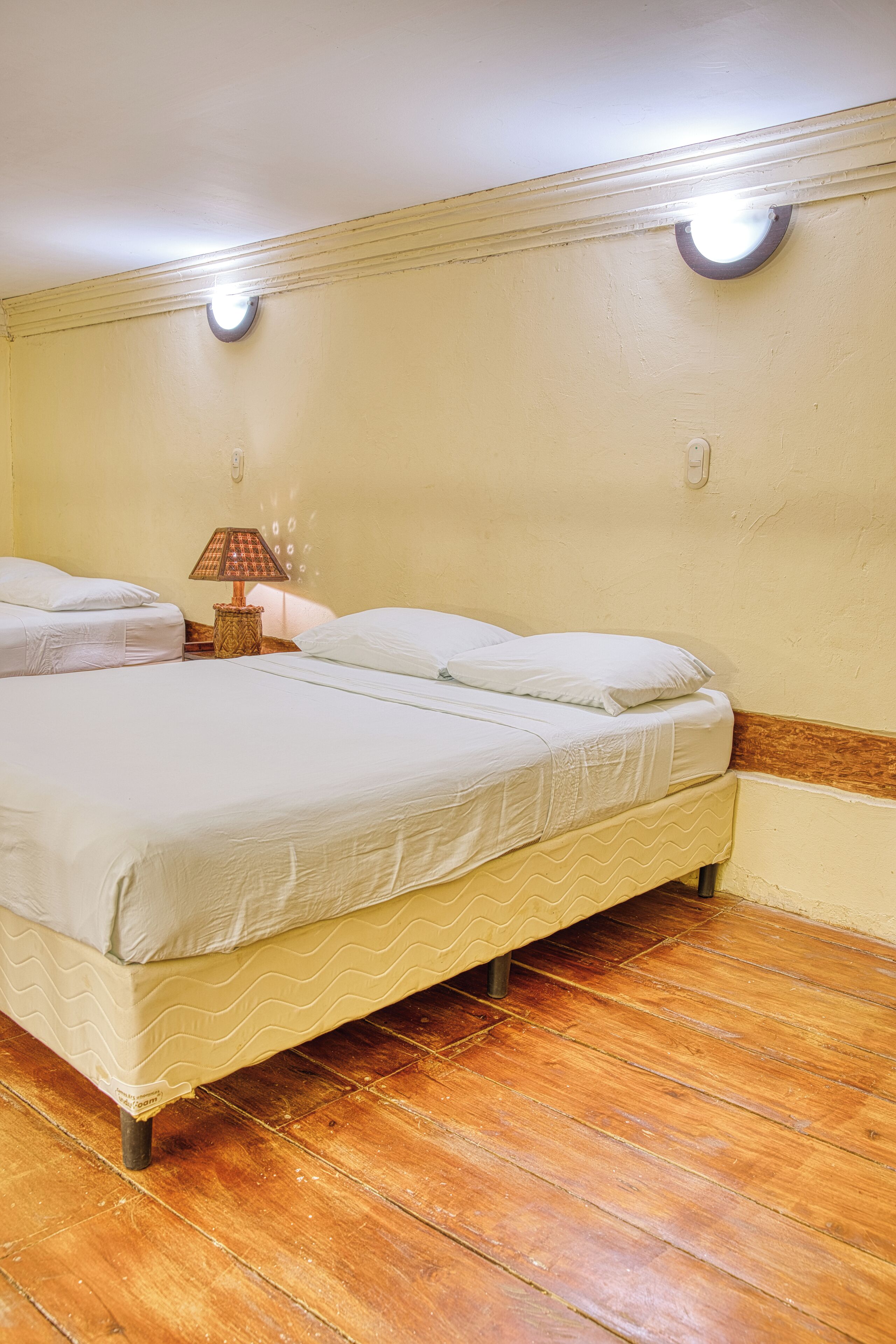 Una habitación con dos camas, una lámpara y suelo de madera.