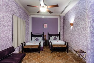 Una habitación con dos camas, un ventilador de techo, una mesita de noche y una lámpara de pared.