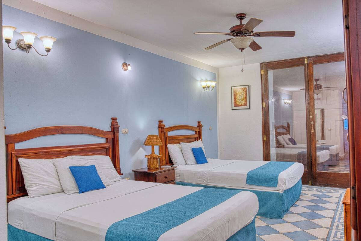 A room with two beds, a ceiling fan, wall sconces, and a tiled floor.