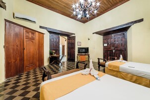 Quarto de hotel com duas camas, uma televisão, uma escrivaninha e uma cadeira, e portas de madeira.