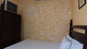 Un dormitorio con una cama, ventilador de techo, aire acondicionado, un televisor sobre un mueble y un cuadro en la pared.