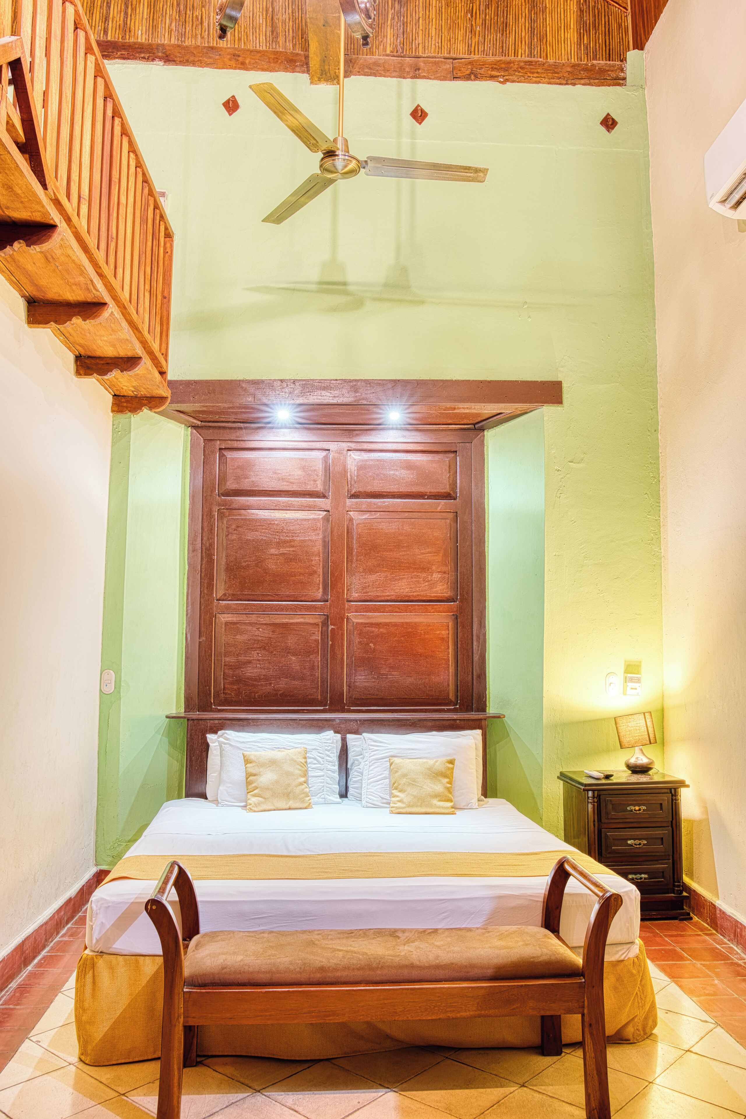A bedroom with a large bed, wooden headboard, a ceiling fan, a nightstand, and a bench.
