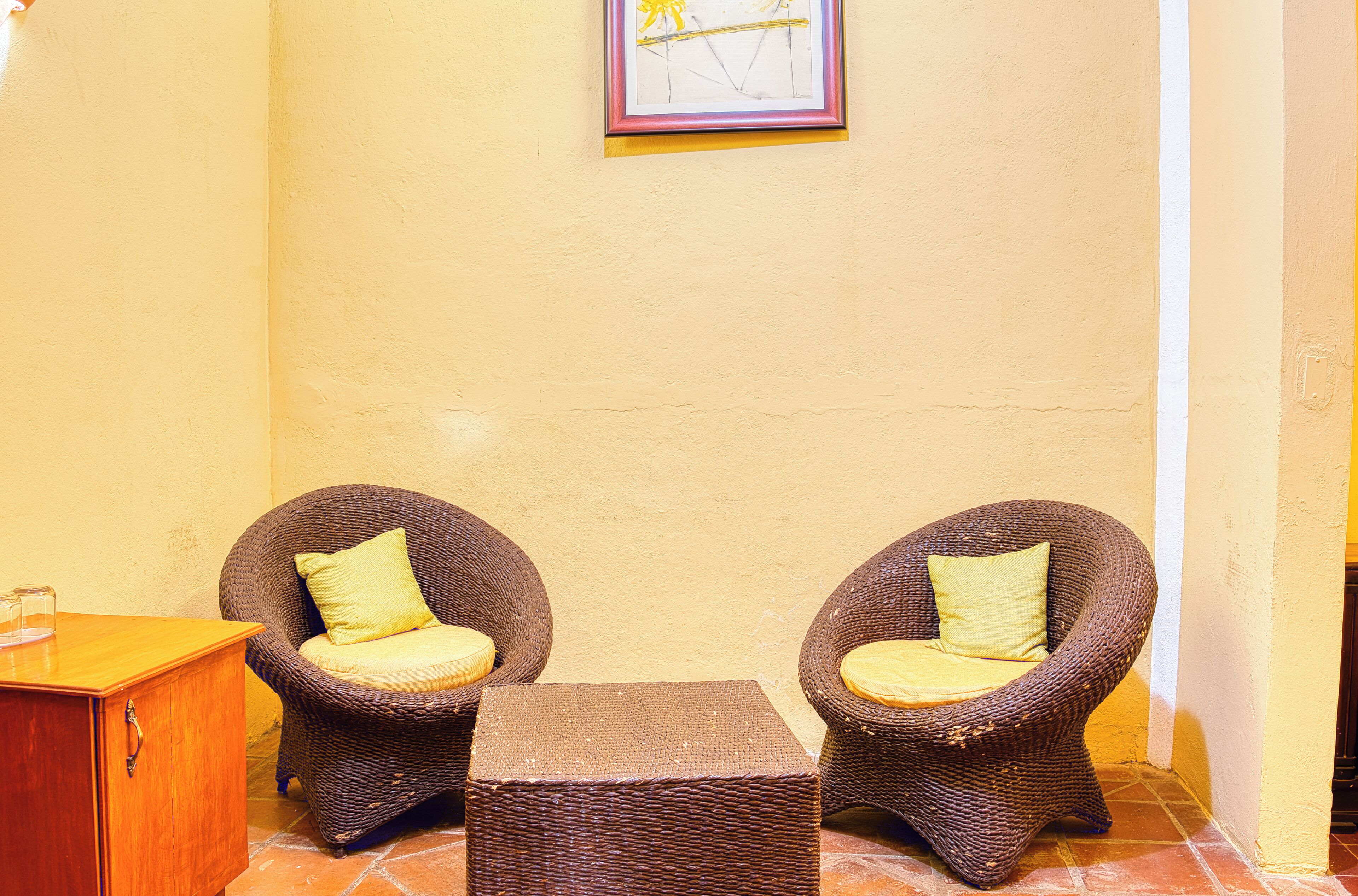Two wicker chairs with cushions, a small wooden table, and a framed picture on the wall.