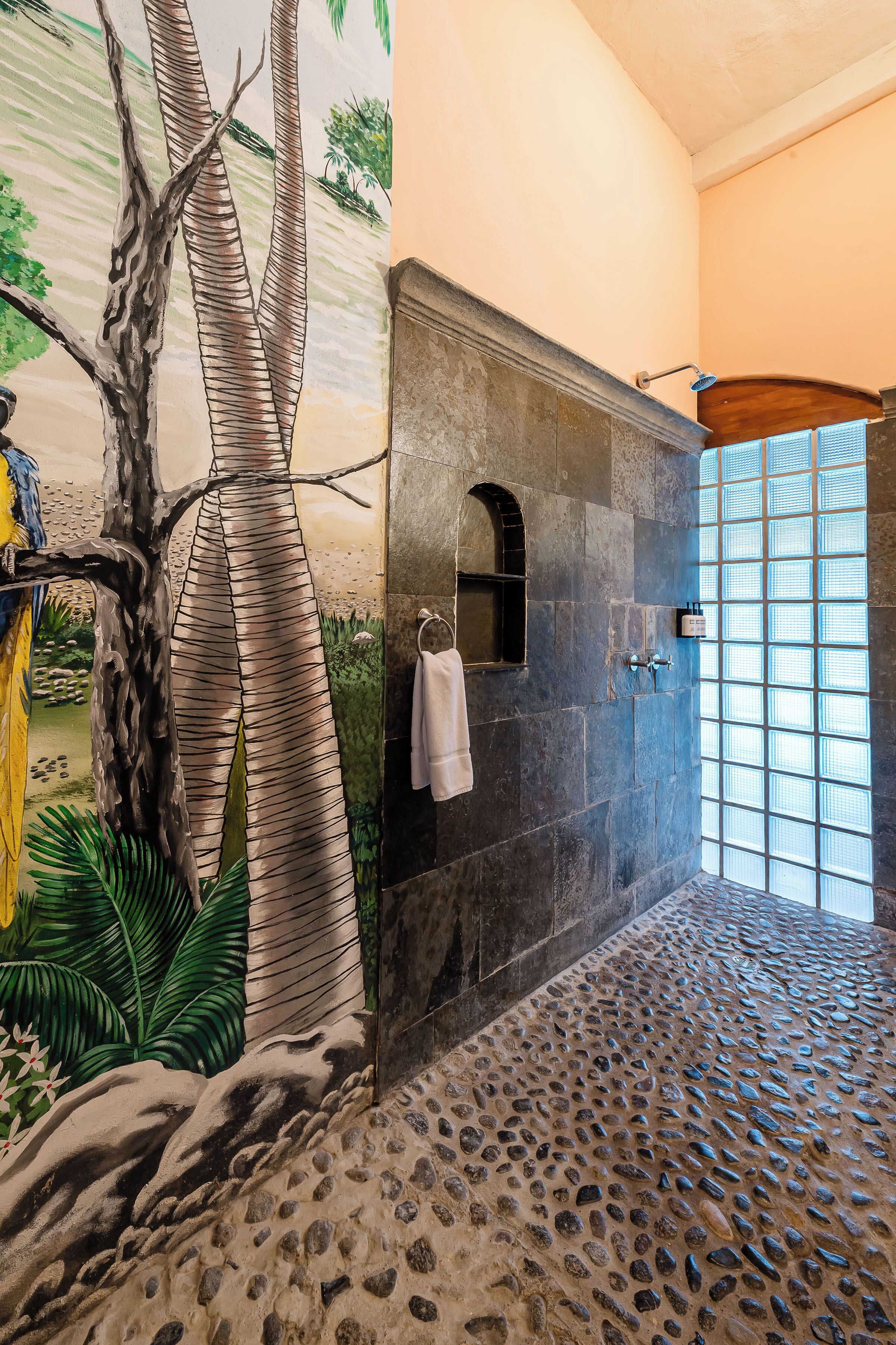 A bathroom with a stone wall, a shower area, and a mural of a tree and foliage.