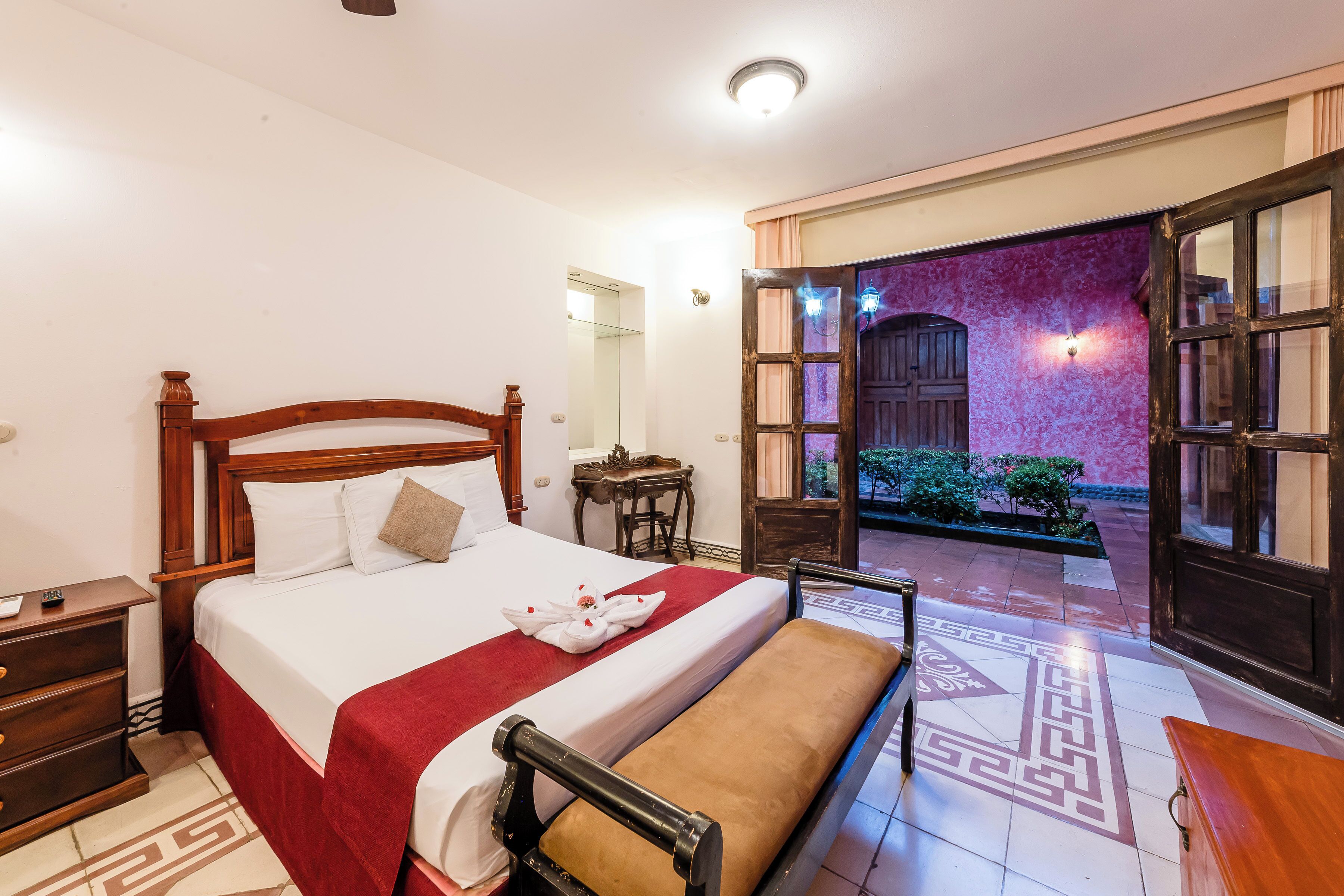 A hotel room with a bed, bedside table, and a view of the outside.