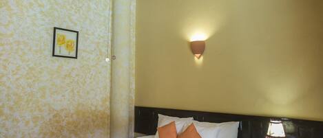 A hotel room with a bed, a ceiling fan, a nightstand, and a wall-mounted light.