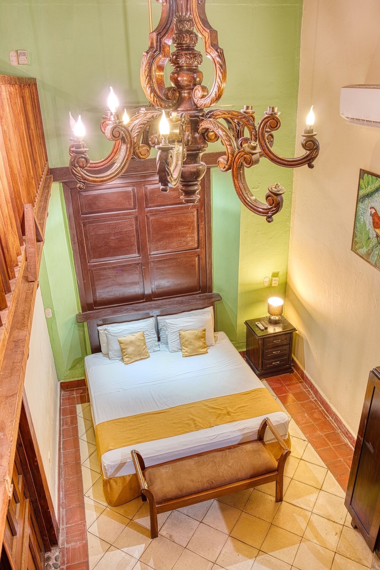 A bedroom with a wooden bed, a chandelier, a bedside table, and a green wall.