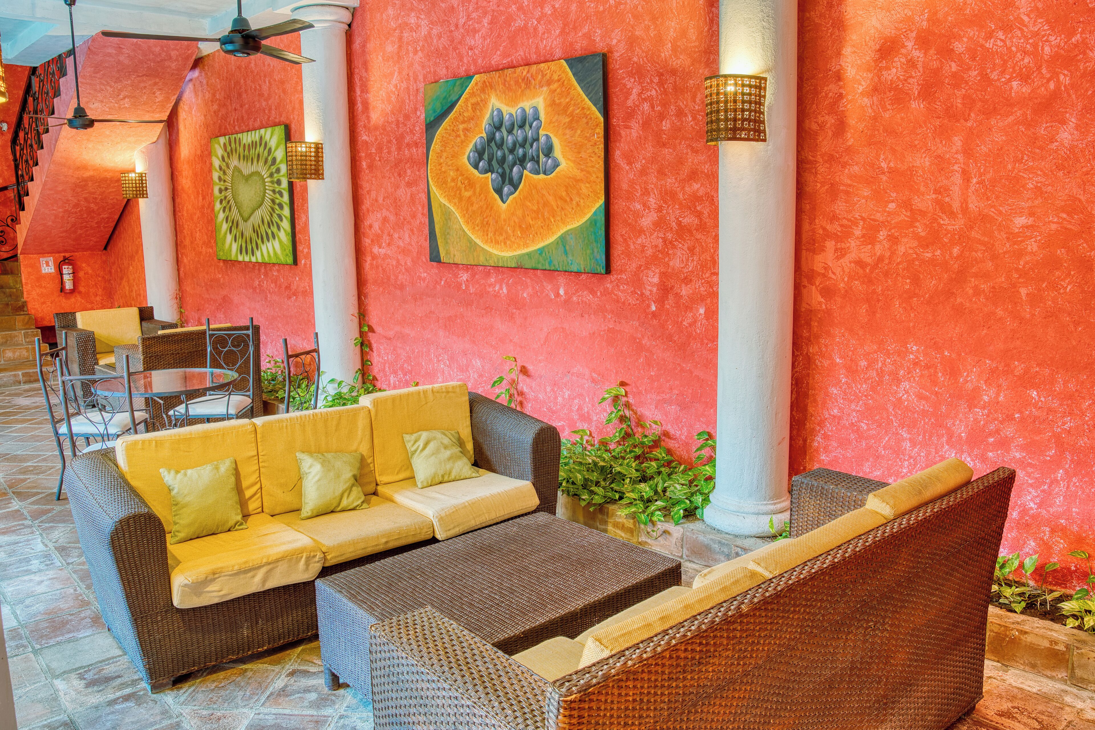 A lobby with a red wall, wicker furniture, and a ceiling fan.