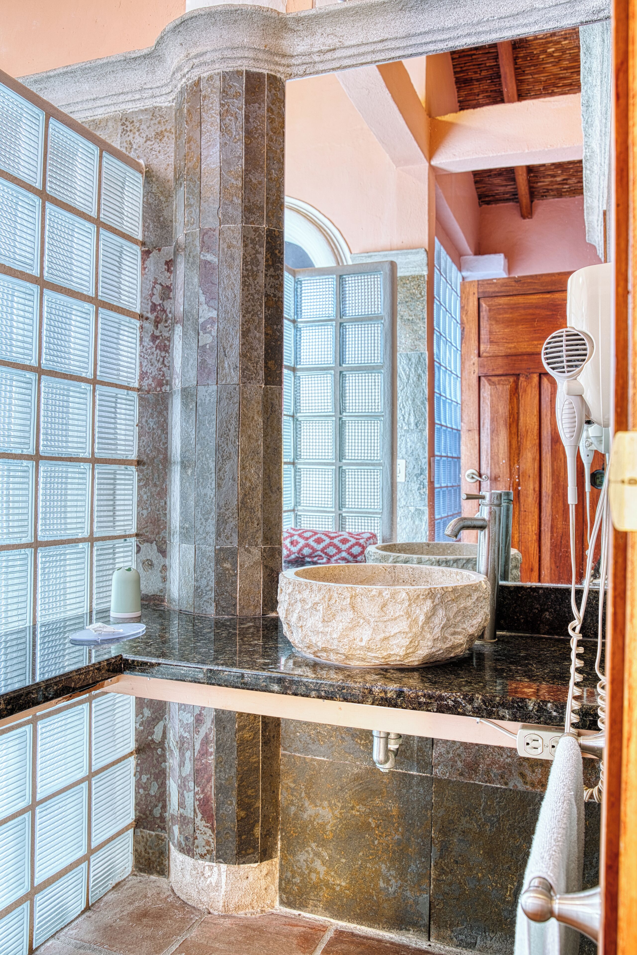 A bathroom with a stone sink, a hairdryer, and a window with a view.
