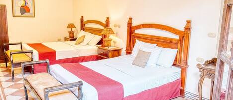 A hotel room with two beds, a wooden headboard, a patterned floor, and a painting on the wall.