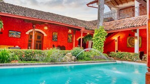Un bâtiment rouge doté d’une piscine, d’un espace couvert surmonté d’un toit rouge et d’un escalier menant à un balcon.