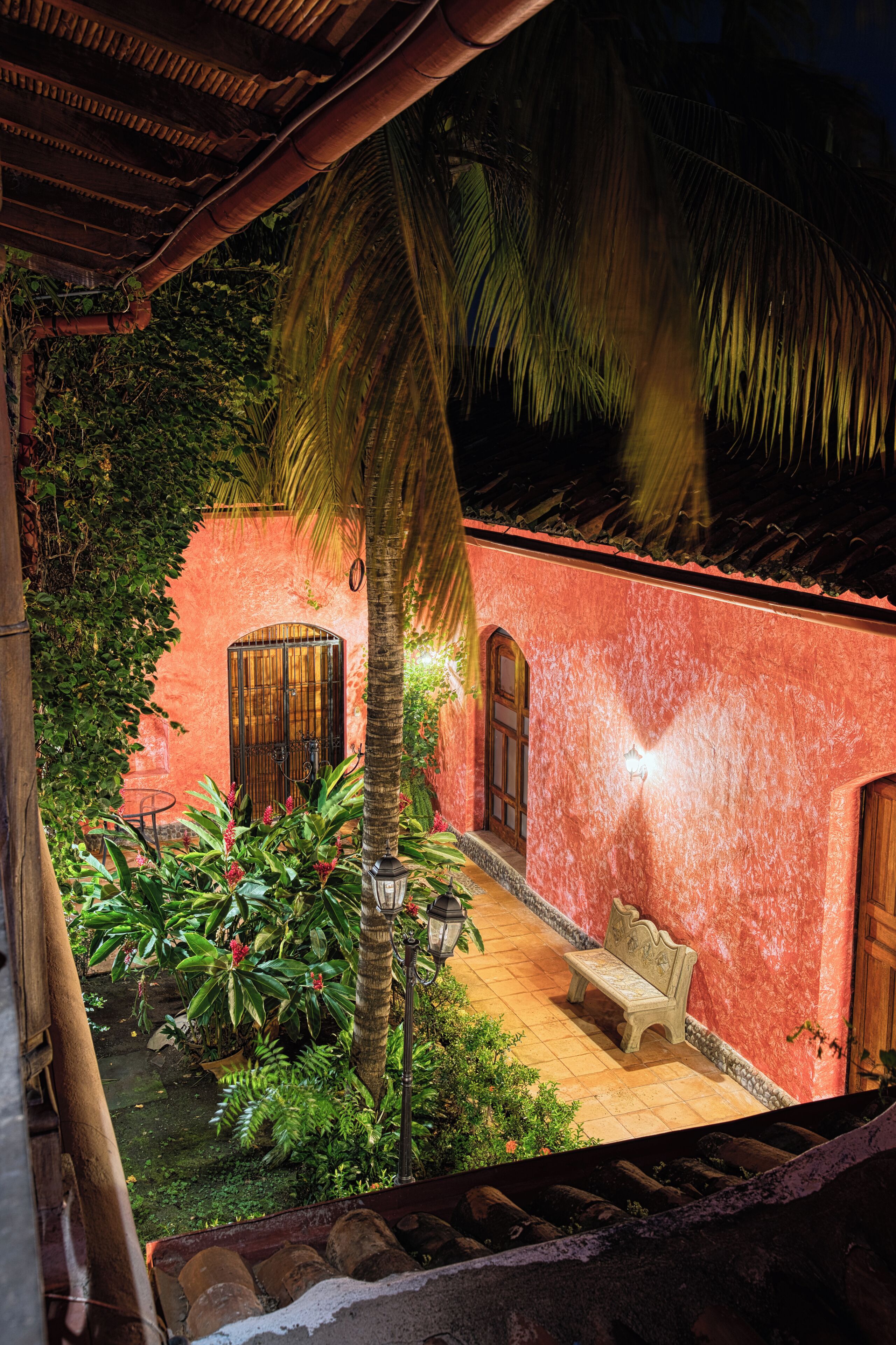 A courtyard with a bench, a palm tree, and a building with a red wall and a door.