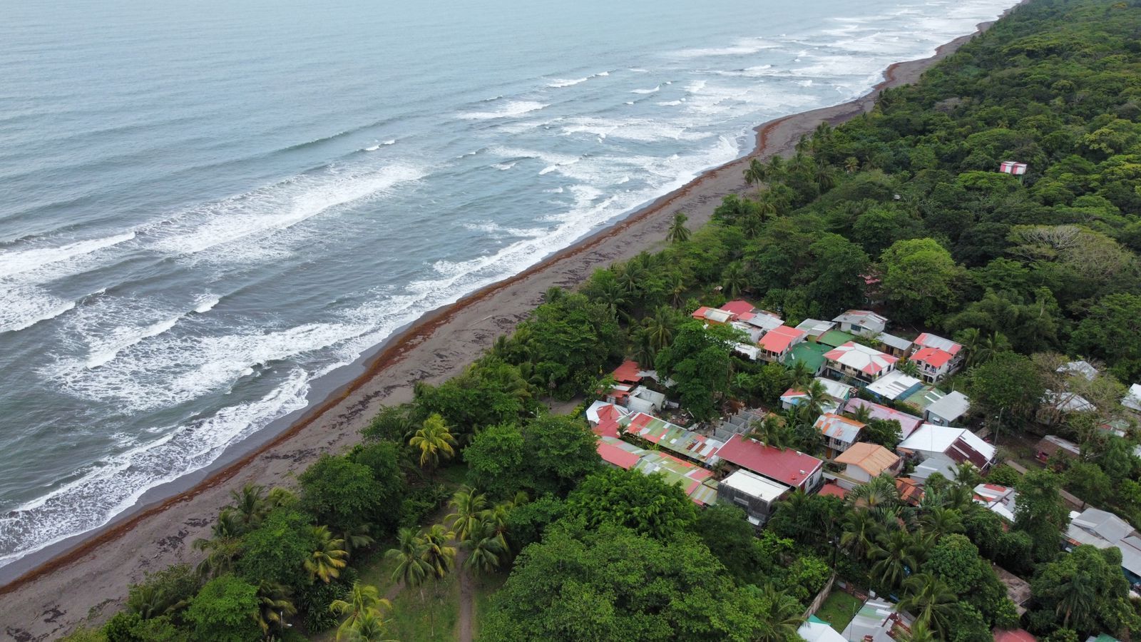 An aerial view of a coastal area with a beach and a cluster of buildings with colorful roofs.