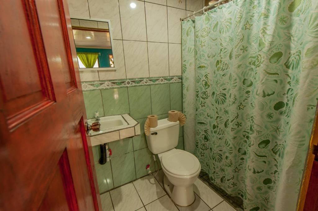 Une salle de bain avec des toilettes, un lavabo et un rideau de douche à motifs verts.