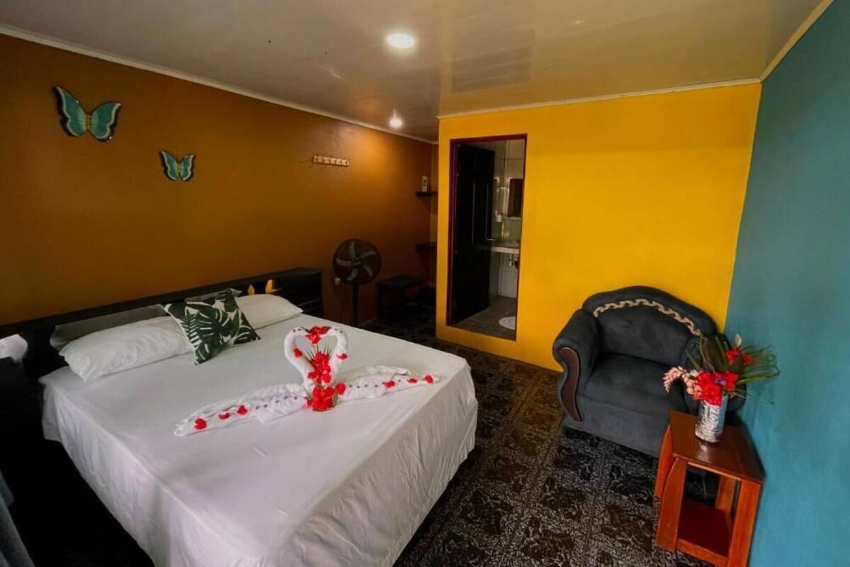 A hotel room with a bed, a chair, a small table with a vase, and butterfly wall decorations.